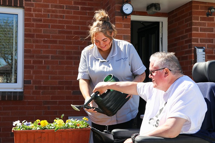 gofalwr yn helpu cleient i ddyfrio blodau